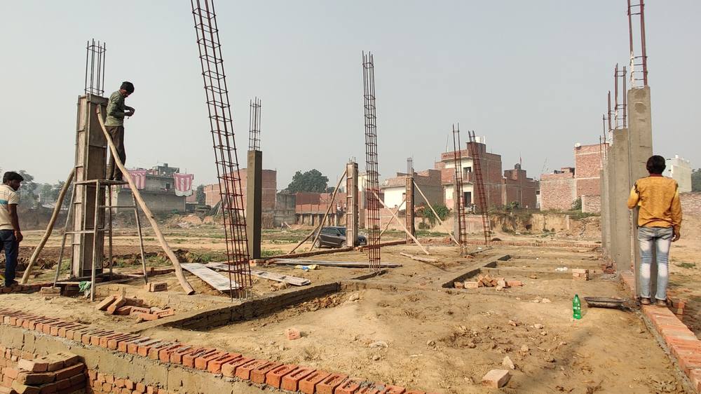 Column reinforcement cages standing above cast columns, with plinth brickwork laid along the line of the walls.